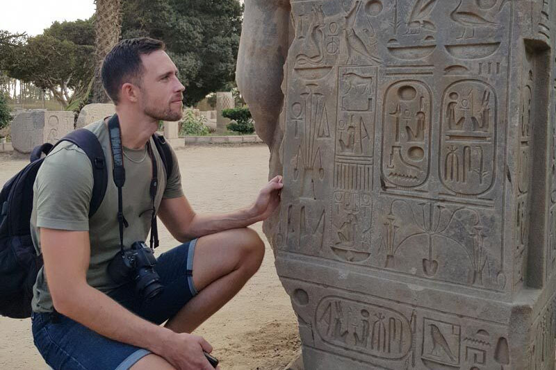 Junger Mann betrachtet in der Hocke eine Tafel mit Hieroglyphen