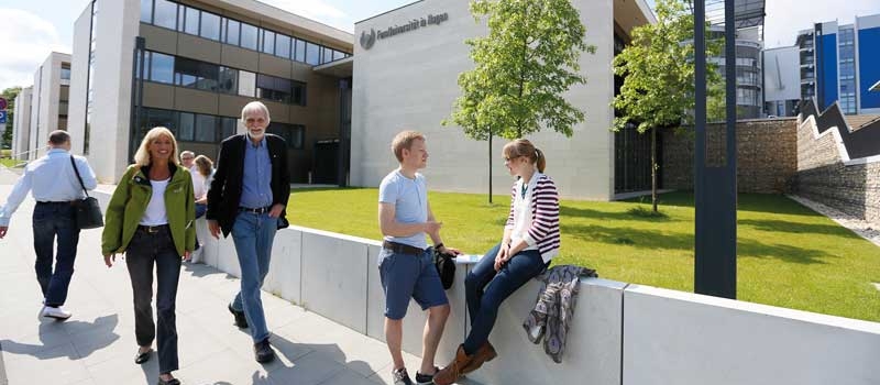 Mehrere Personen bewegen und unterhalten sich auf dem Campus der FernUniversität in Hagen. Im Hintergrund zu sehen ist das Gebäude des Kutlur- und Sozialwissenschaften. 