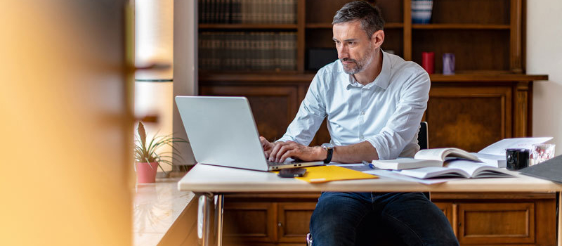 Ein Mann sitzt am Schreibtisch und schaut auf den Laptop.