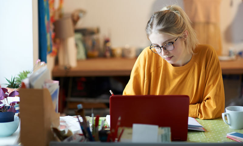 Eine junge Frau sitzt am Schreibtisch vor einem aufgeklappten Laptop.
