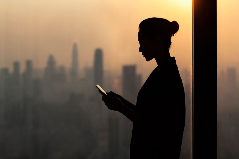 Eine Frau steht mit ihrem Smartphone vor einer Skyline.