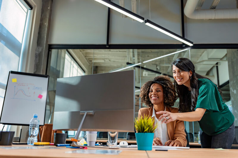 Zwei Frauen sitzen an einem PC und arbeiten zusammen